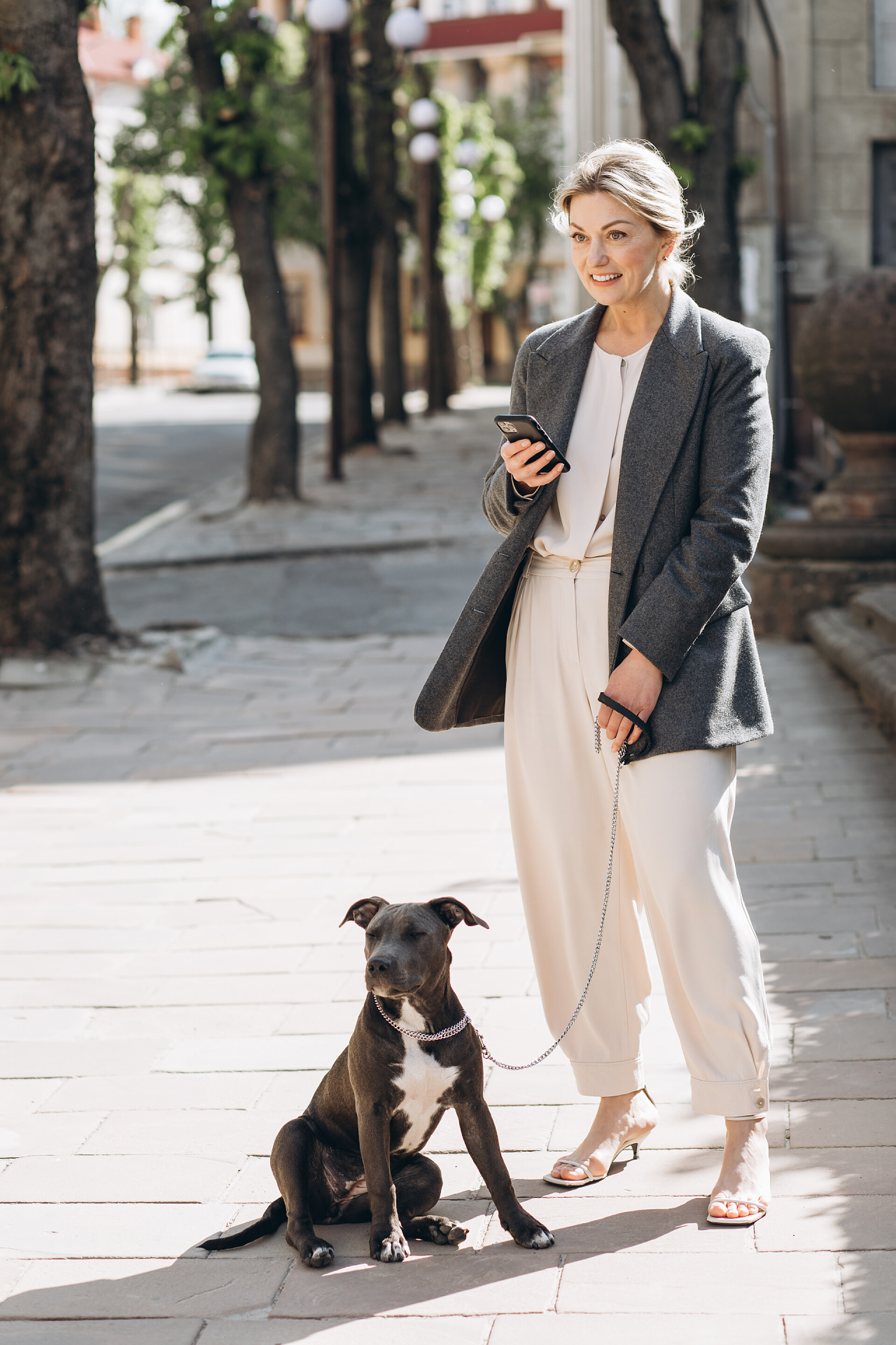 穿着灰色夹克的成熟金发女商务人士微笑着遛狗退休生活外国女人
