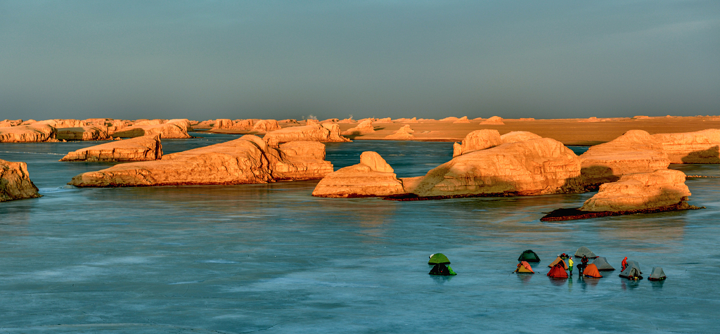 青海海西水上雅丹红色的山丘与冰冻的湖面上露营的游客