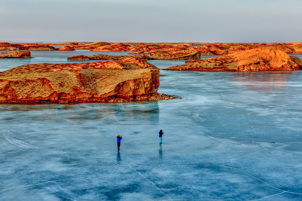 青海海西水上雅丹红色的山丘与冰冻的湖面上的游客