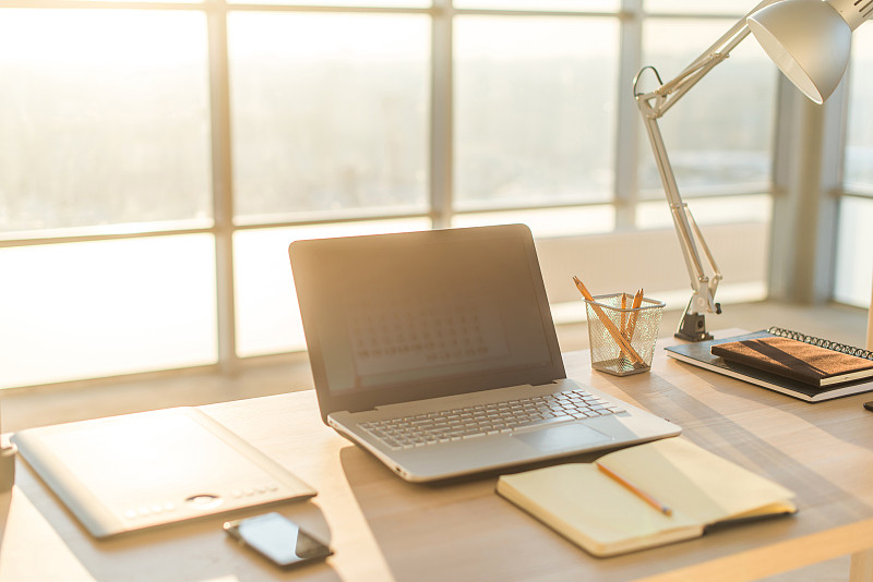 侧视图图片的工作室工作与空白笔记本，笔记本电脑。舒适的工作台，家庭办公室。