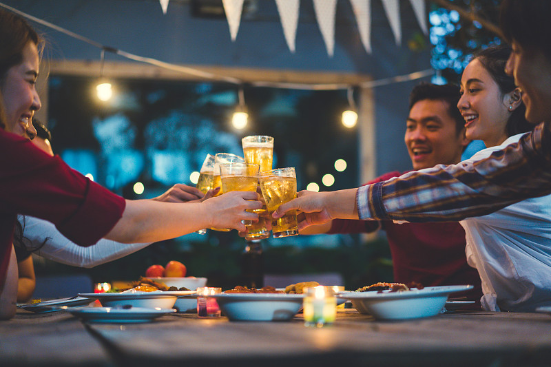 亚洲人庆祝节日，他们碰杯，啤酒和晚餐快乐