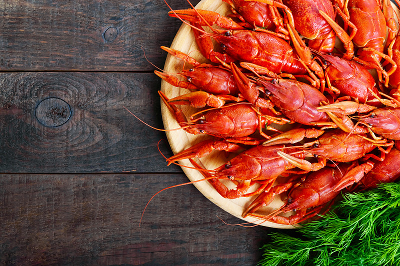 一堆美味的煮小龙虾放在一个圆木托盘上，放在一张黑色的桌子上。前视图。为题字预留空间。