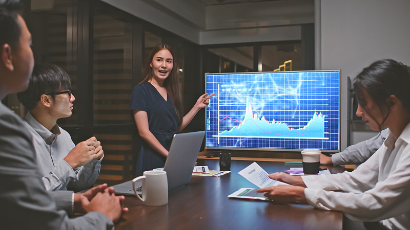 年轻的亚洲女商人带领商务财务团队在战略会议上发言，在办公室工作到深夜。营销策略分析，股票市场交易，或者团队合作