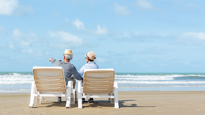 亚洲生活方式的老年夫妇拥抱和指着沙滩幸福的爱情浪漫和放松的时间。老年人旅游、家庭旅游、退休后的度假和夏季休闲活动。