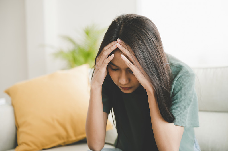 因工作或人际关系问题而沮丧的亚洲女性，坐在沙发上，感到绝望和焦虑，孤独，有心理问题