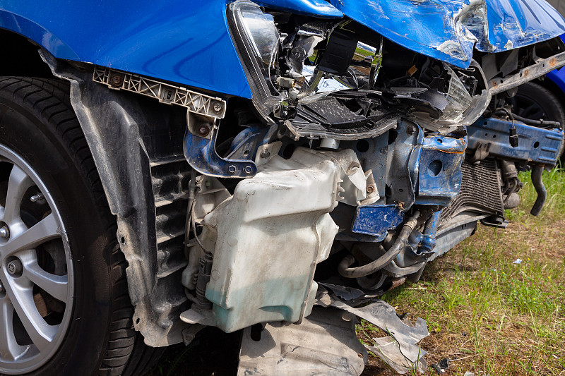 一辆被毁坏的汽车在迎头相撞后被毁坏:一个皱巴巴的散热器，一个轮子和一个坏掉的前灯