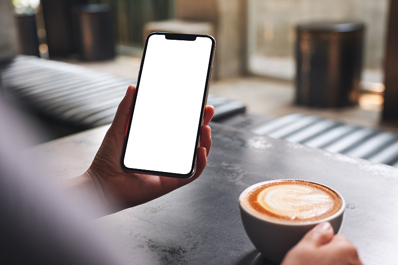 一个女人拿着手机和空白的桌面屏幕喝咖啡