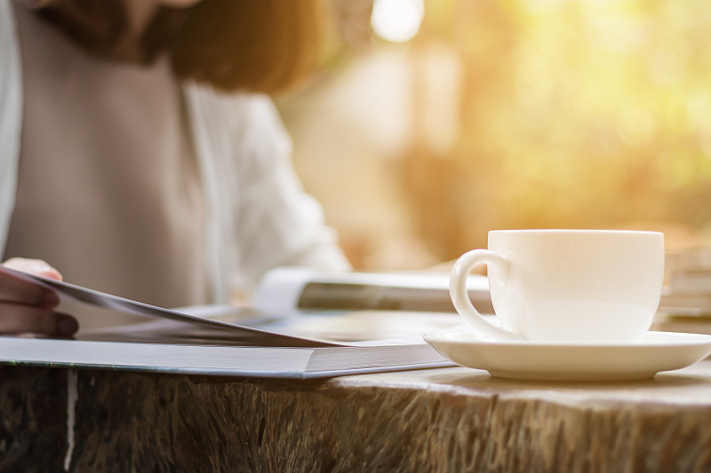 一个女人正在花园里看书和喝咖啡。