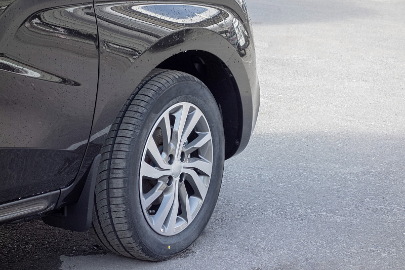 前轮上的轮辋特写在一个新的灰色跨界雨滴后。潮湿的人行道上。