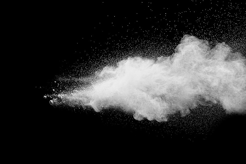 在黑色背景上发射白色粒子飞溅。在黑暗的背景下出现了奇异的白色粉末爆炸云。