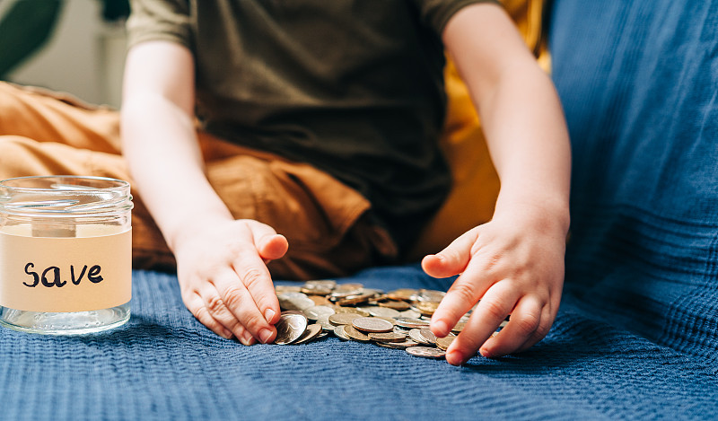 近距离的小男孩的手抓和把堆栈硬币在玻璃罐与保存标签。捐赠、省钱、慈善、家庭理财计划理念