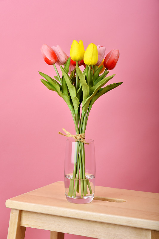 粉红色背景的郁金香花束。木桌花瓶里插着人工郁金香。