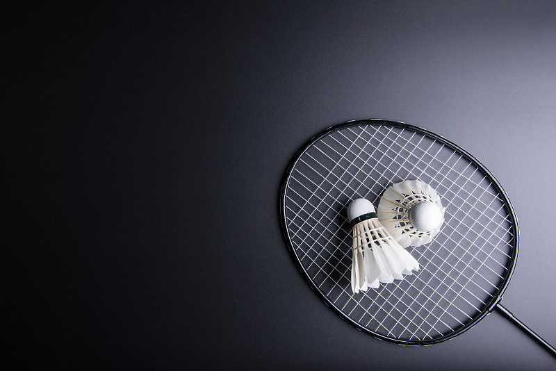 黑色背景上的两个羽毛球和羽毛球拍。运动概念，复制空间图像为您的文本。