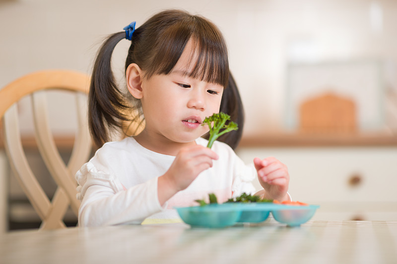 年轻的女孩在真实的厨房背景下吃新鲜的绿色蔬菜