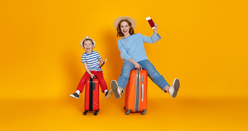 旅途愉快!家庭旅行者母亲和孩子手提箱，票和护照在黄色背景
