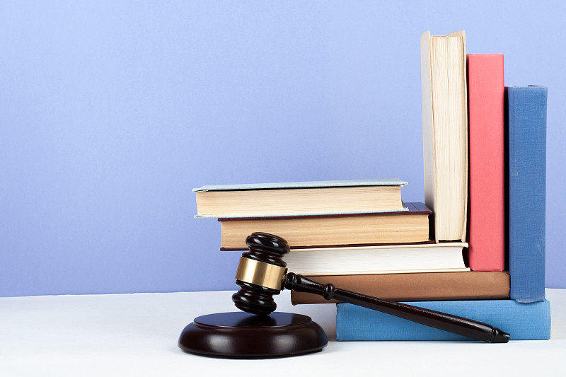 法律概念翻开书与木制法官木槌在法庭或执法办公室的桌子上，蓝色背景。复制文本空间。