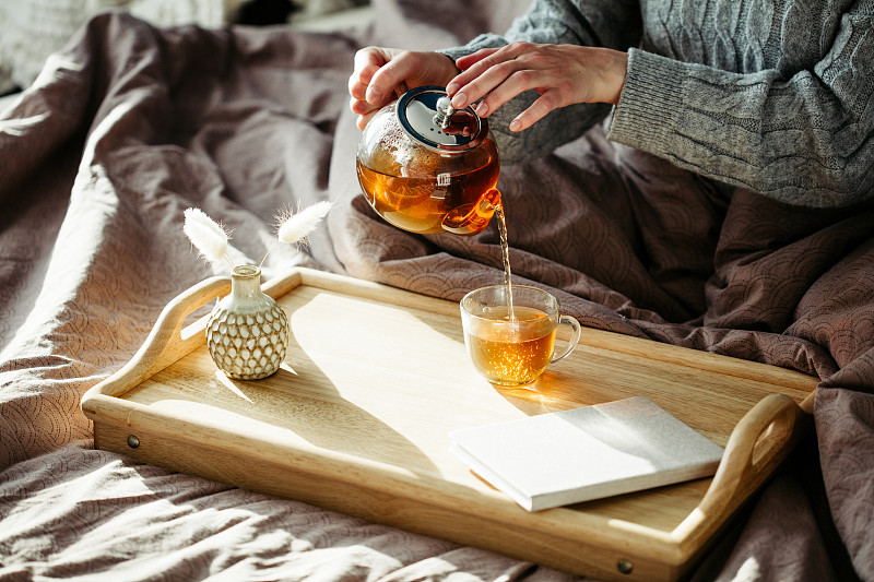 女人从茶壶里往杯子里倒茶。舒适的家，hygge风格的室内。