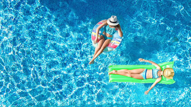 孩子们在游泳池上空无人机观看，快乐的孩子们在充气圈和床垫上游泳，活泼的女孩们在度假胜地的家庭度假水中玩得很开心