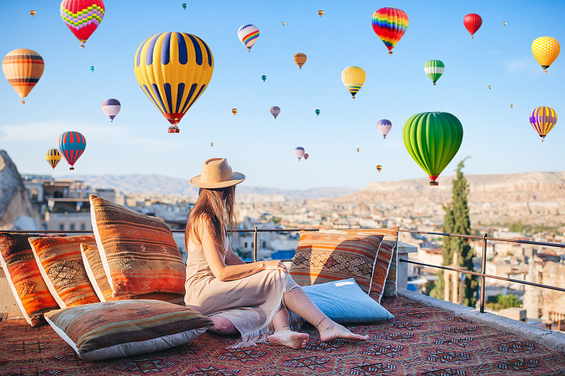 土耳其卡帕多西亚，日出时快乐的年轻女子在看热气球