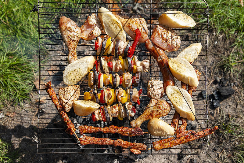 壁炉上烘烤零食的特写镜头。肉和蔬菜串，面包卷和鸡肉。