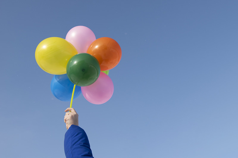 手持飞行的氦气球，对抗着明亮的蓝色天空。副本的空间。