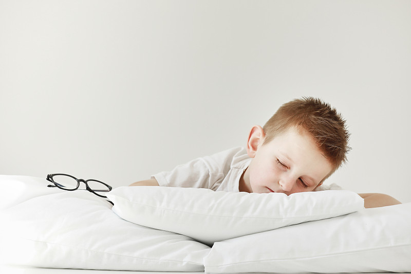 可爱的小男孩睡在床上。早上在白色的床上做梦。侧面的眼镜