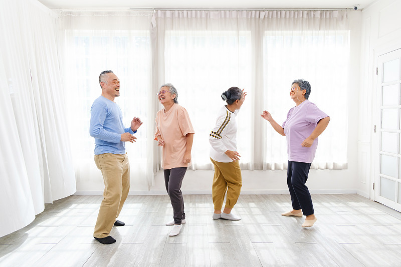 活跃的亚洲老年群体混合男女锻炼，一起在家里跳舞放松，微笑和大笑。适合成熟老年人和退休人士的室内活动。