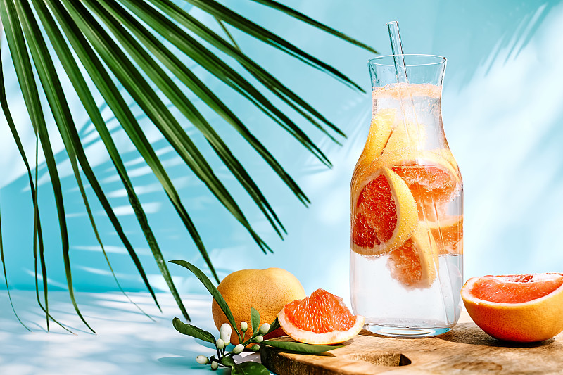 夏日鸡尾酒里有葡萄柚、迷迭香和多汁的柑橘类水果片。新鲜健康的葡萄柚饮料在阳光下与阴影。创意饮料在蓝色柔和的背景。