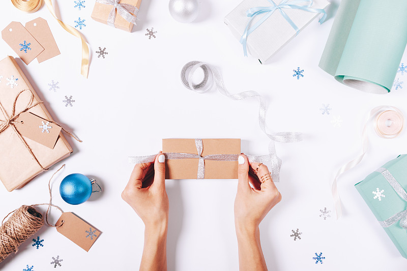 女性的手在盒子上系一个蝴蝶结，上面有礼物