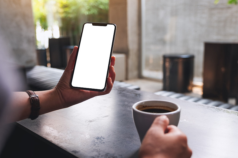 一个女人拿着手机和空白的桌面屏幕喝咖啡