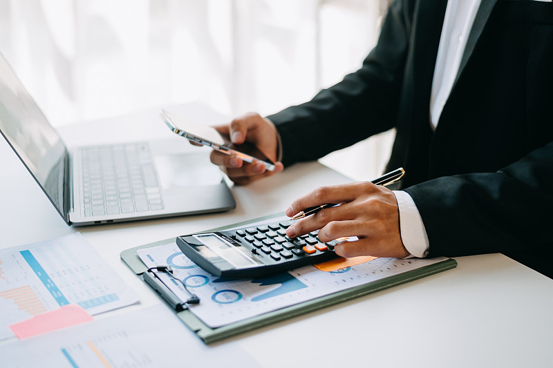 商务文件放在办公桌上，配有智能手机和数字平板电脑，图表金融和女性在办公室工作