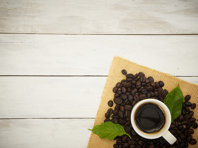 咖啡杯和咖啡豆放在白色厚木板桌上。