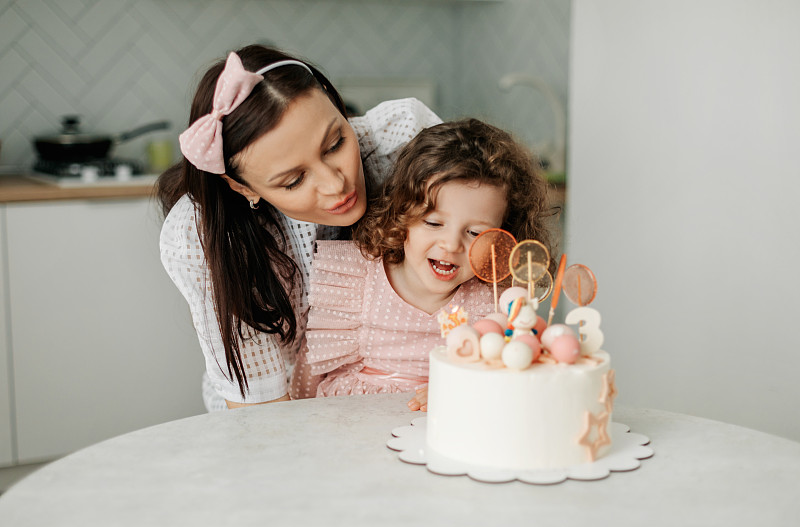 一个可爱的婴儿和她的妈妈吹灭生日蛋糕上的蜡烛。生日,节日,活动