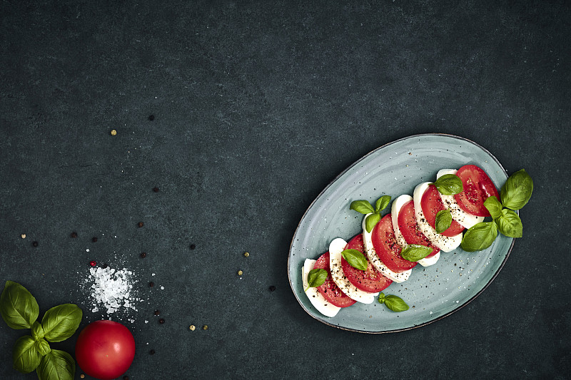 黑色桌子上的椭圆形盘子里有新鲜沙拉