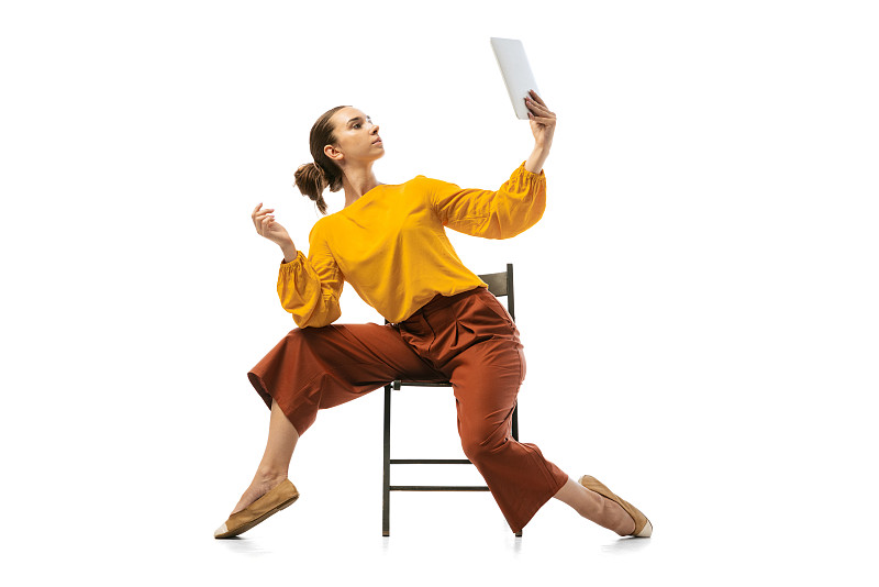 年轻漂亮的女孩的肖像，穿着时髦服装的办公室工作人员在扶手椅上跳舞孤立在白色的工作室背景。美概念、商业、芭蕾、艺术、舞蹈风格