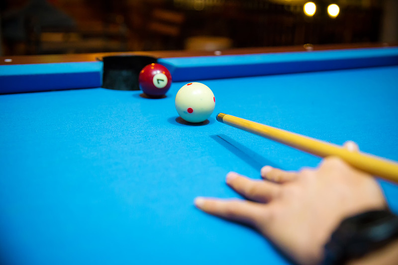 用手和球杆将球放在蓝色的毛毡台球桌上。室内运动。体育和赌博的概念。