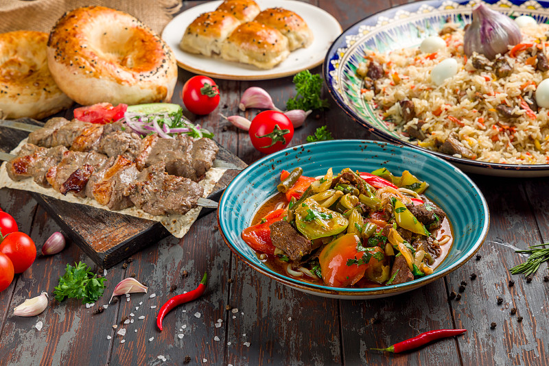 菜的乌兹别克菜lagman，抓饭，串羊肉，面包和蔬菜在旧木桌