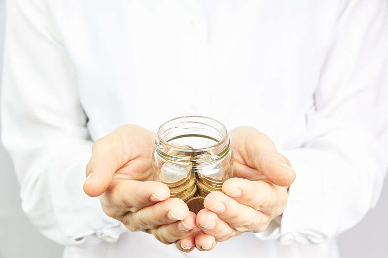 手拿硬币放在玻璃罐里。货币增长，储蓄观念