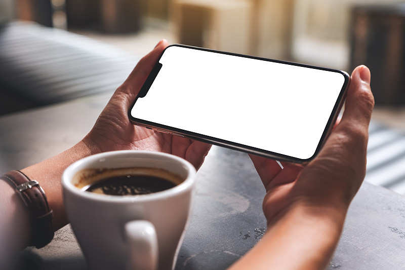 一个女人拿着手机，白色的桌面屏幕和咖啡杯在桌子上