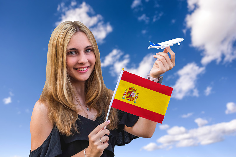 天空背景上，女孩手持西班牙国旗和玩具飞机