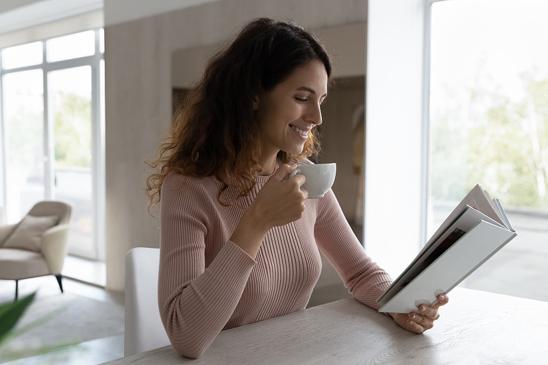 微笑的女人在家里看书，喝茶或咖啡