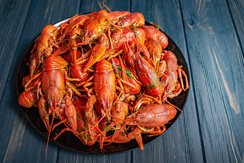 煮小龙虾放在黑色的盘子里，背景是黑色的木头。很多水煮小龙虾。