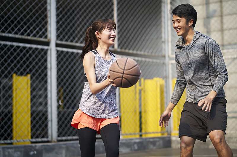 年轻的亚洲夫妇有乐趣打篮球户外