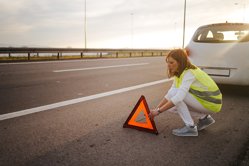 一个女人在她的车抛锚后设置了一个三角形警告。汽车在公路上抛锚了