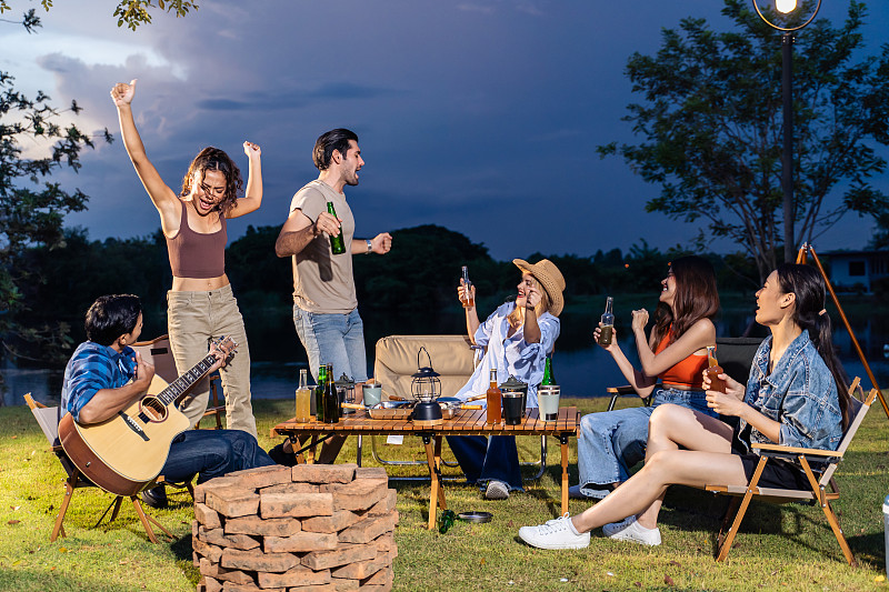 一群不同的朋友一起在帐篷里举行户外露营聚会。有魅力的年轻男女旅行者随着音乐跳舞，享受假日假期在自然木材森林旅行。