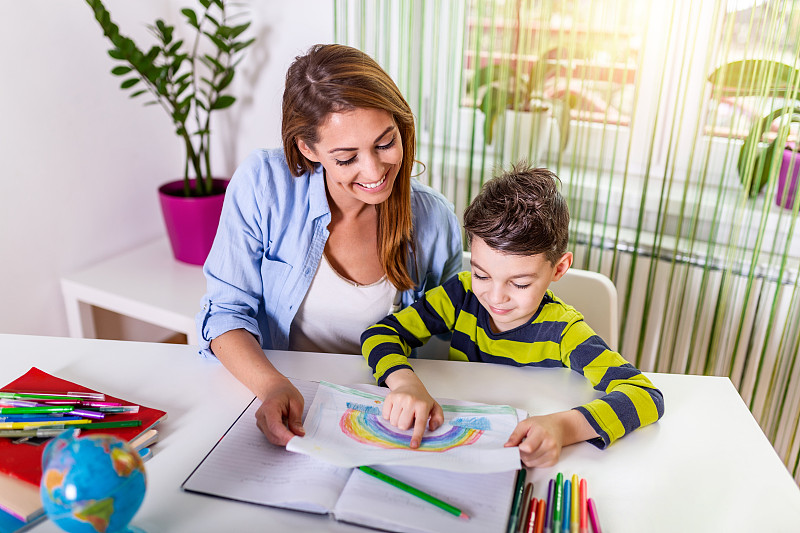 妈妈和儿子在做作业的时候微笑着拥抱着。妈妈在帮小男孩做作业。妈妈帮助孩子做作业。教育与家庭观念