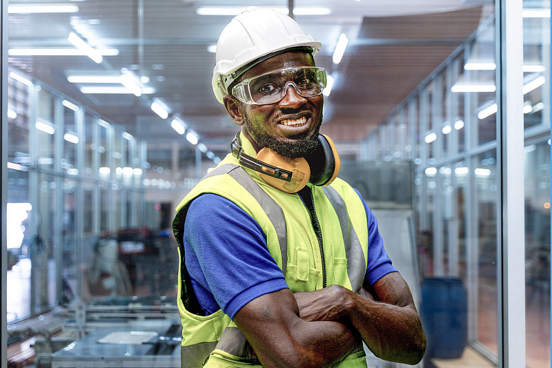 工厂工程师非洲人站着自信的绿色工作服和安全帽。工人在室内玻璃用机械设备技术和洁净工业工厂工作。