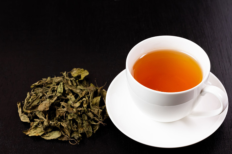 图丝或神圣的罗勒茶在白色的杯子和一堆干图丝叶在黑色的木制背景。