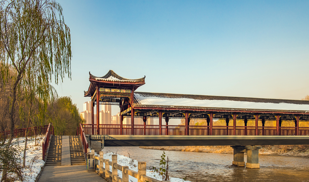 初雪后的晴日蓝天下河流上的长廊桥覆盖了白雪