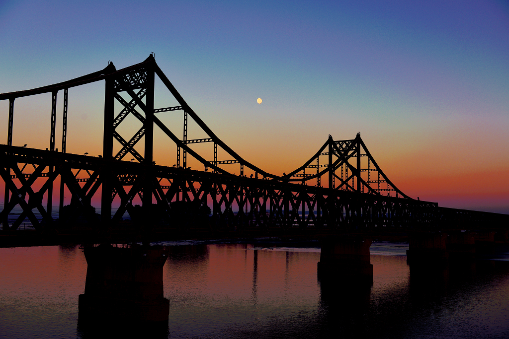 日落后的天空挂着月亮鸭绿江大桥的剪影